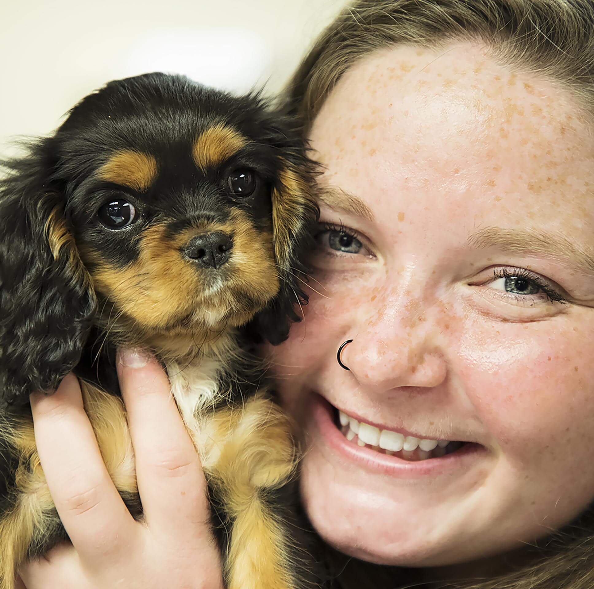 Veterinary Patient Care Team member, Michelle snuggling a black, tan and white Cavalier King Charles Spaniel