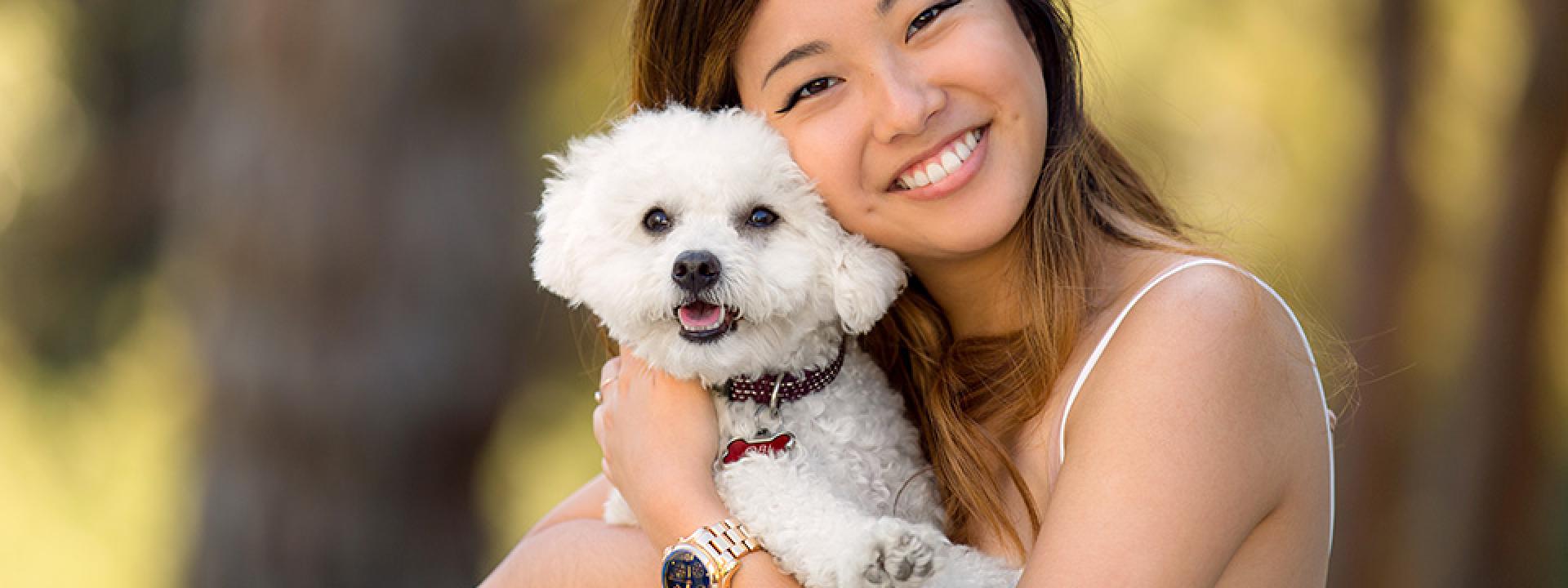 Young woman smiling while hugging white poodle-type dog